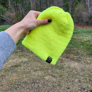 May include: A bright neon yellow knit beanie with a black label that reads "WURDE PROJECTED".
