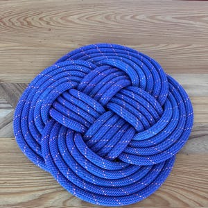 Puede incluir: Una cuerda azul y naranja atada en un nudo grande e intrincado. El nudo es plano y circular, asemejándose a una flor.