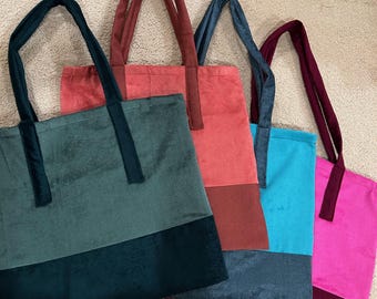 May include: Four tote bags in shades of green, red, blue, and pink. Each bag has a contrasting colour block at the bottom and matching handles. The bags are made of a soft, velvety material.