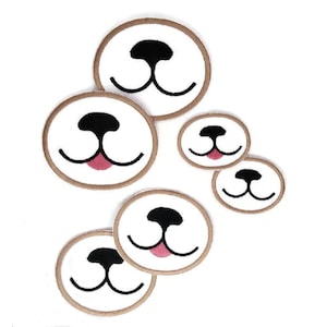 May include: Five brown felt dog face patches with white faces and black noses. The patches are in different sizes and some have pink tongues.