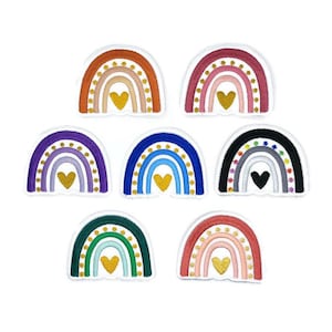 Può includere: Otto toppe di arcobaleno ricamate con un cuore dorato al centro. Ogni arcobaleno ha uno schema di colori diverso, tra cui viola, blu, verde, arancione, rosa e nero.