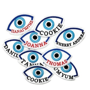 May include: Ten white and blue eye-shaped patches with different names embroidered on them, including "Cookie", "Joanna", "Sherry Andrea", "Panagiotis", "Daniel", "Thomas", and "Um Yum".