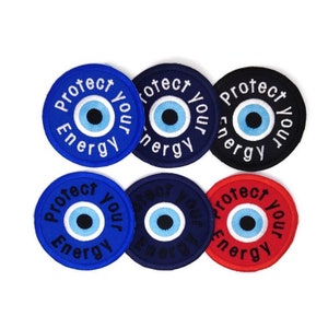 Könnte beinhalten: Sechs runde gestickte Patches mit einem blauen bösen Auge und dem Text "Protect Your Energy" in weißen Buchstaben. Die Patches befinden sich auf einem weißen Hintergrund. Die Patches sind in Blau, Dunkelblau, Schwarz und Rot.
