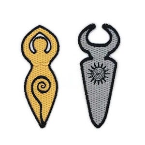 Op de afbeelding: Twee geborduurde patches met spirituele symbolen. Eén is goudkleurig met een zwarte omtrek, met een figuur met opgeheven armen en een spiraal. De andere is grijs met een zwarte omtrek, met een zonnesymbool en een halve maanvorm.