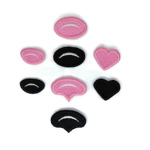 Puede incluir: Un conjunto de parches bordados en varias formas, incluyendo óvalos, corazones y una forma única que se asemeja a una boca. Los parches son principalmente rosas y negros, con detalles bordados en blanco. Están dispuestos sobre un fondo blanco.