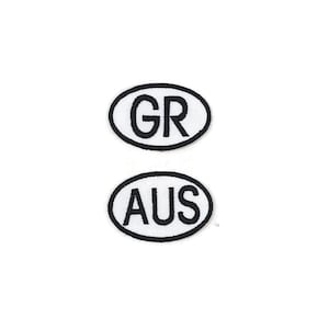 May include: Two embroidered patches with black borders and white backgrounds. The top patch has "GR" in black letters, and the bottom patch has "AUS" in black letters. Both patches are oval-shaped.