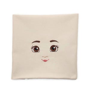 Könnte beinhalten: Ein quadratisches, cremefarbenes Kissen mit gestickten Gesichtszügen. Das Design umfasst braune Augen mit langen Wimpern, geschwungene Augenbrauen und einen kleinen, lächelnden rosa Mund. Das Kissen ist wahrscheinlich dekorativ.