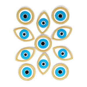 Puede incluir: Doce parches bordados con el símbolo del mal de ojo. Los parches tienen la forma de un ojo con un iris azul y una pupila negra, rodeados por un círculo blanco y un contorno dorado. Algunos parches son redondos, mientras que otros son ovalados.