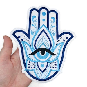 May include: A blue and white embroidered hamsa hand with an evil eye in the center. The hamsa is a symbol of protection and good luck.