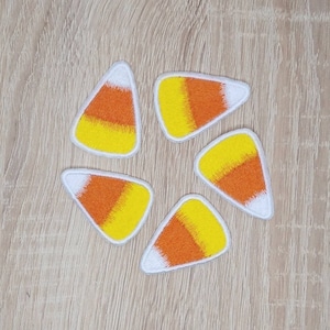 May include: Five felt iron-on patches shaped like candy corn. The patches are white, orange, and yellow.