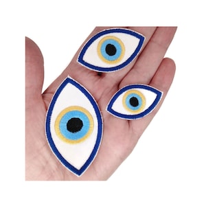 Peut inclure: Trois patchs œil bleu maléfique de différentes tailles. Les patchs sont blancs avec un motif d'œil bleu, bleu clair et or. Les patchs sont brodés et ont un contour bleu.