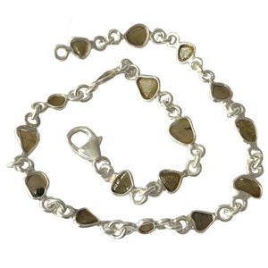 May include: A silver bracelet with a chain link design and multiple small, irregular, light brown stones.