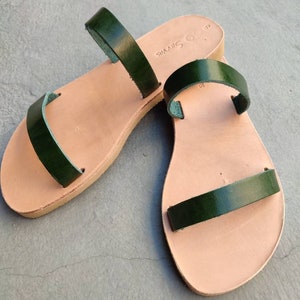 May include: A pair of green leather sandals with two straps on each sandal. The sandals have a light brown leather sole.