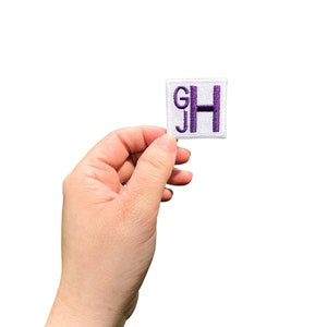 May include: A white square patch with the letters "GH" embroidered in purple.