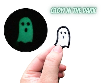 May include: White ghost-shaped iron-on patch with black outline. The patch glows in the dark and is shown glowing green in a separate image.