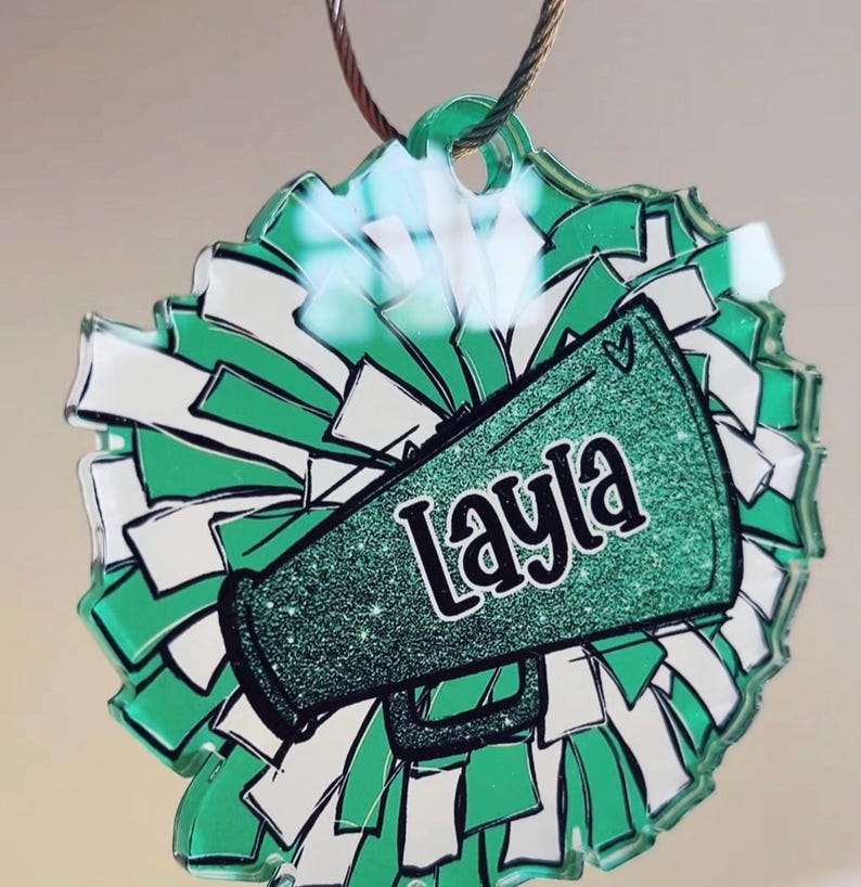 May include: Green and white cheerleading pom-pom ornament with a green glitter megaphone that says "Layla" on it.