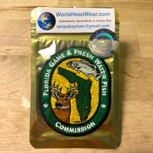 May include: Green embroidered patch with the Florida state outline, a deer, and a fish. The text reads "Florida Game & Fresh Water Fish Commission".