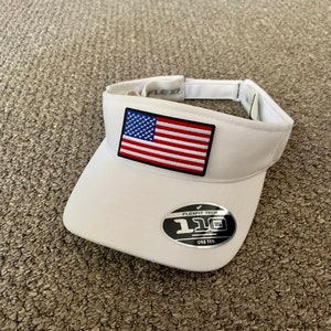 May include: White visor with a small American flag patch and a Flexfit Tech One Ten logo.
