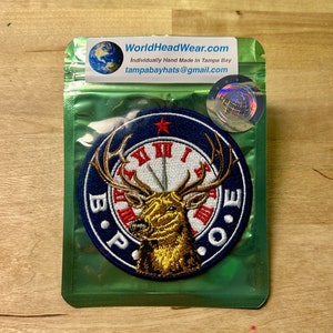 May include: A blue and white embroidered patch with a deer head and clock face. The deer has a red nose and antlers. The clock face has Roman numerals and the words "B.P.O.E." around the edge. The patch is in a clear plastic bag.