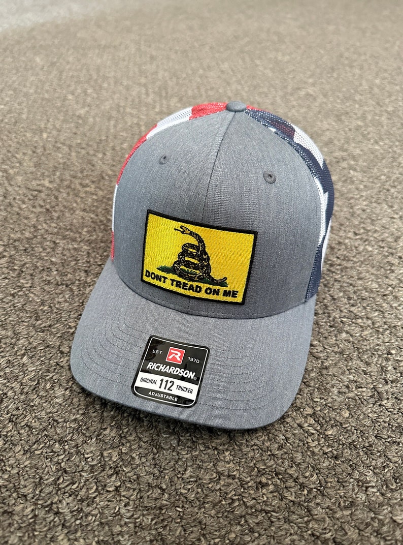 May include: A gray and red trucker hat with a yellow patch that says "Don't Tread On Me" and a green snake. The hat has a black label that says "Richardson" and "Original 112 Trucker Adjustable".