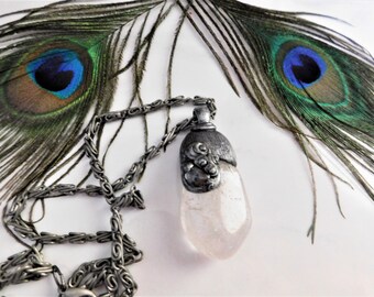 May include: A silver chain necklace with a clear quartz pendant. The pendant has a silver cap with a floral design. The necklace is displayed on a white background with peacock feathers.