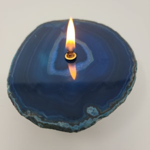 May include: A blue agate slice with a small, round, gold-colored candle holder in the center. A flame is burning in the candle holder.
