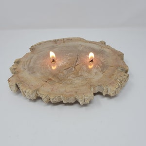 May include: A wooden candle holder with a natural, light brown finish. The holder is shaped like a tree stump and has two small, round candle holders on top. The candles are lit and casting a warm glow.