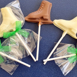 May include: Five chocolate ice skate lollipops wrapped in clear plastic bags with green ribbon bows. The lollipops are in two colours: white chocolate and milk chocolate.