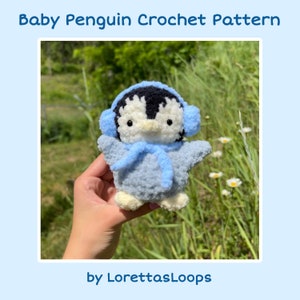 May include: A crocheted baby penguin wearing blue earmuffs and a blue scarf. The penguin is holding its wings out and is sitting in a hand. The background is a field of green grass and white flowers.