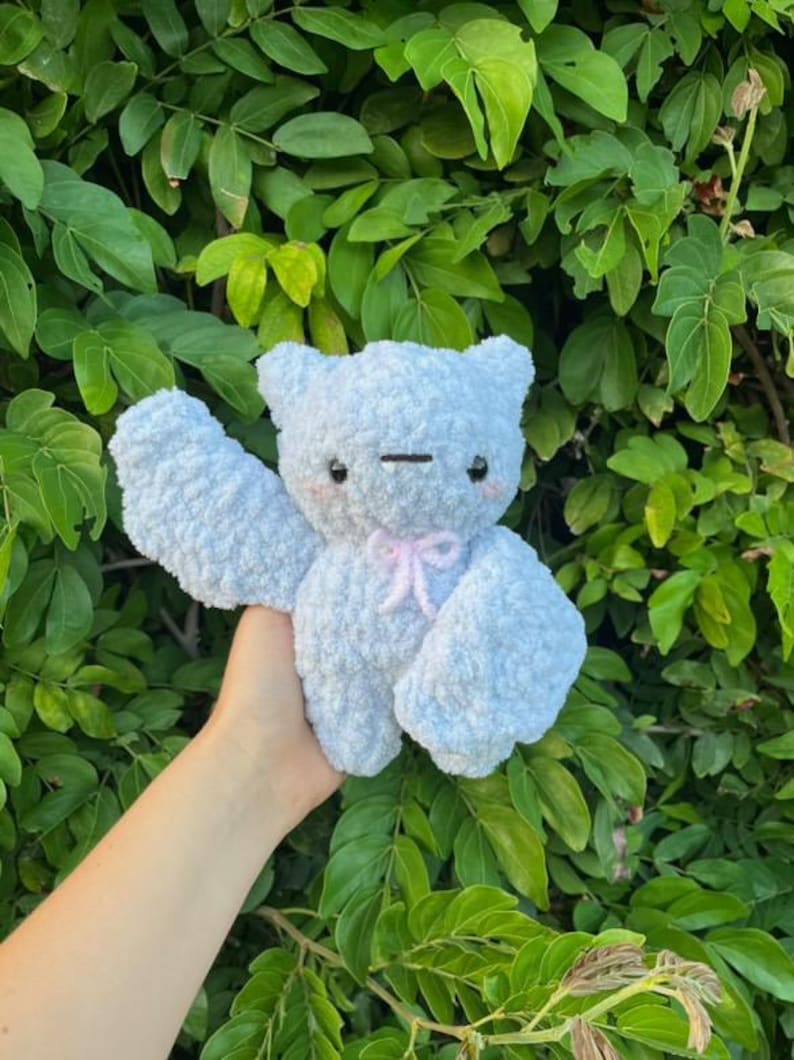 May include: A light blue plush toy bear with a pink bow. The bear has a stitched smile and large, black eyes.