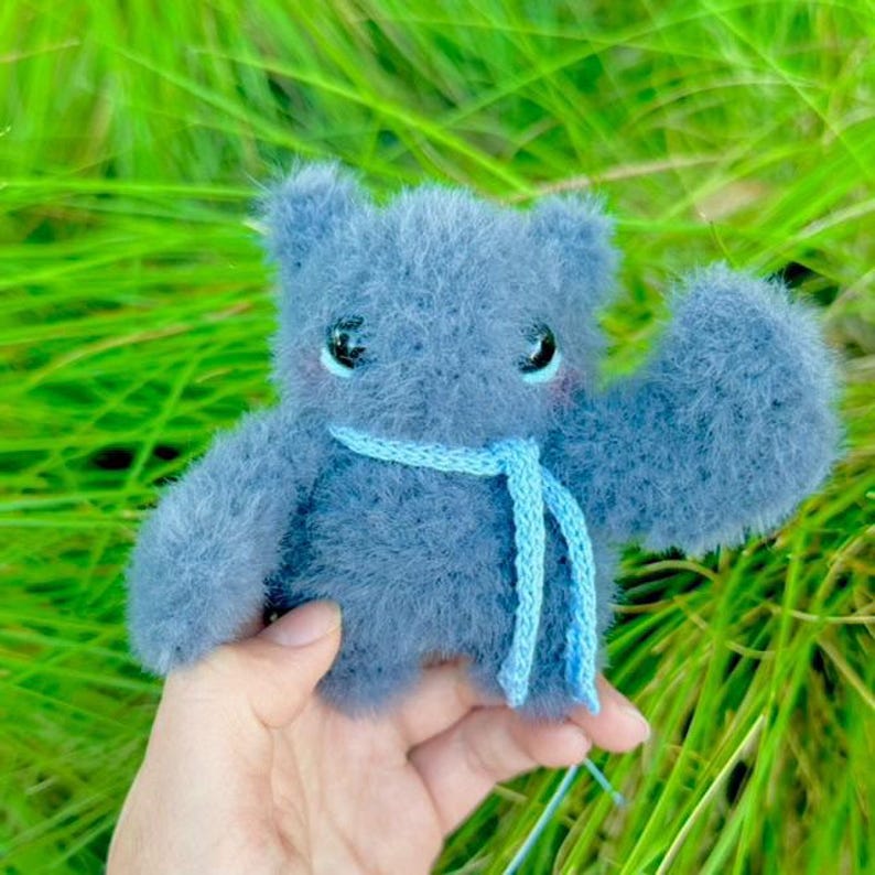 May include: A small, gray, fuzzy plush toy with a blue scarf. The toy has large, black eyes and a sweet expression.