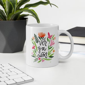 Puede incluir: Taza de cerámica blanca con un diseño floral y el texto "Ver ga ción" en letras negras.