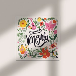 May include: A square print featuring the word "Venezuela" in black script, surrounded by colorful illustrations. The design includes flowers, a pink ukulele, a bird, and a cartoon figure, all set against a white background.