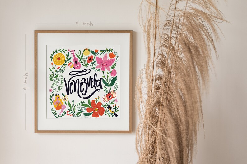 May include: A framed 9-inch square art print featuring the word "Venezuela" in cursive, surrounded by colorful flowers, a guitar, and a bird. The artwork has a white background and is in a wooden frame.