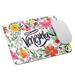 Puede incluir: Un ratón de ordenador blanco con un diseño floral colorido y la palabra "Venezuela" en escritura negra. El diseño incluye flores, hojas, pájaros e instrumentos musicales.
