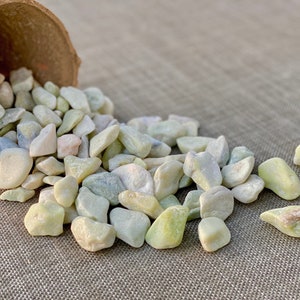May include: A pile of small, smooth, white and green stones spilling out of a brown pot onto a beige fabric surface.