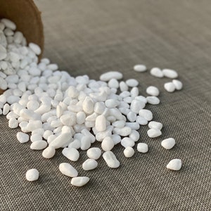 May include: A close-up of white decorative stones spilling out of a brown pot onto a gray textured surface.