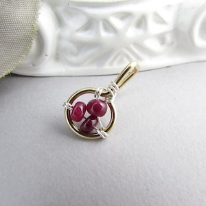 May include: A gold wire wrapped pendant with three red ruby gemstones.