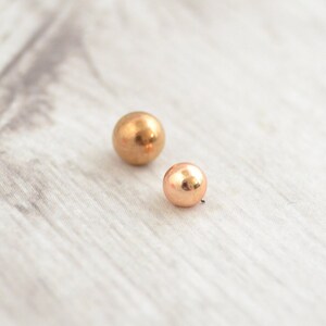 May include: Two gold-colored metal balls of different sizes. The larger ball is on the left and the smaller ball is on the right.