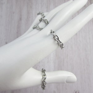 May include: A set of three silver chain rings. The rings are worn on the index, middle, and thumb fingers of a hand.