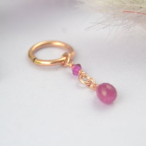 May include: A rose gold hoop earring with a pink gemstone dangle. The dangle features a small pink crystal and a larger pink gemstone.
