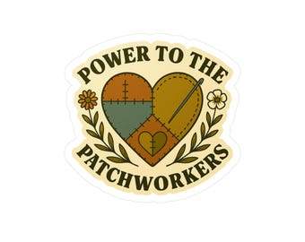 Könnte beinhalten: Ein Aufkleber mit einem herzförmigen Patchwork-Design in Braun-, Grün- und Goldtönen, mit Nadel und Faden. Der Text "POWER TO THE PATCHWORKERS" ist kreisförmig um das Herz angeordnet, mit floralen Akzenten.