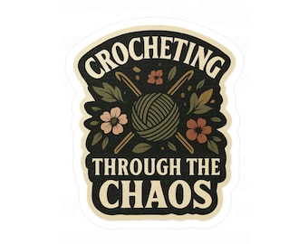Könnte beinhalten: Ein Aufkleber mit cremefarbenem Rand mit dem Text "CROCHETING THROUGH THE CHAOS". Das Design umfasst einen Wollknäuel, Häkelnadeln, Blumen und Blätter in Grün-, Braun- und Pfirsichtönen.