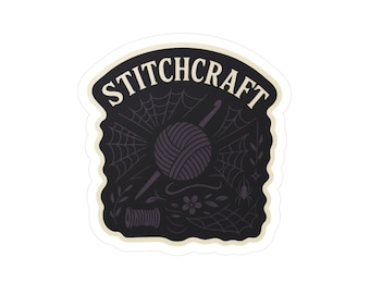 Op de afbeelding: Een sticker met het woord "STITCHCRAFT" in een gebogen, gebroken witte lettertype. Het ontwerp bevat een donkere achtergrond met een spinnenweb, een bol wol, een haaknaald en andere ambachtelijke elementen.