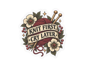 Könnte beinhalten: Ein Aufkleber mit einem dunkelroten Wollknäuel, zwei Stricknadeln sowie weißen Blüten und grünen Blättern. Ein beigefarbenes Banner in der Mitte zeigt den schwarzen Schriftzug "KNIT FIRST, CRY LATER" mit kleinen Sternen.