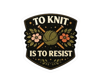 Könnte beinhalten: Aufkleber mit dem Text "TO KNIT IS TO RESIST" in Weiß auf schwarzem Hintergrund. Das Design umfasst einen Wollknäuel, Stricknadeln und florale Elemente in Grün, Pfirsich und Braun.
