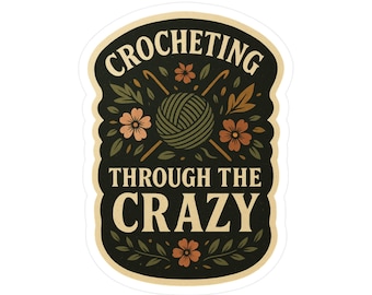 Könnte beinhalten: Ein Aufkleber mit dem Text "CROCHETING THROUGH THE CRAZY" in einem cremefarbenen und dunkelgrünen Farbschema. Das Design umfasst einen Wollknäuel, Häkelnadeln, Blumen und Blätter, alles im Vintage-Stil.