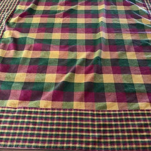 May include: A rectangular fabric tablecloth featuring a large-scale plaid pattern in shades of deep burgundy, forest green, and golden yellow. The central section has wide checks, while the border displays a smaller, tighter checkered pattern.