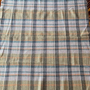 K&ouml;nnte beinhalten: Eine gewebte Decke mit einem Karomuster in Gr&uuml;n, Blau, Orange und Grau. Die Decke hat einen Fransenrand und ein klassisches Karomuster. Die Farben sind ged&auml;mpft, was ihr einen Vintage- oder rustikalen Look verleiht.