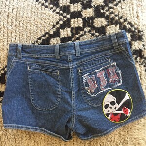 May include: Blue denim shorts with a skull and crossbones patch and a distressed patch that says "VIP" on the back.